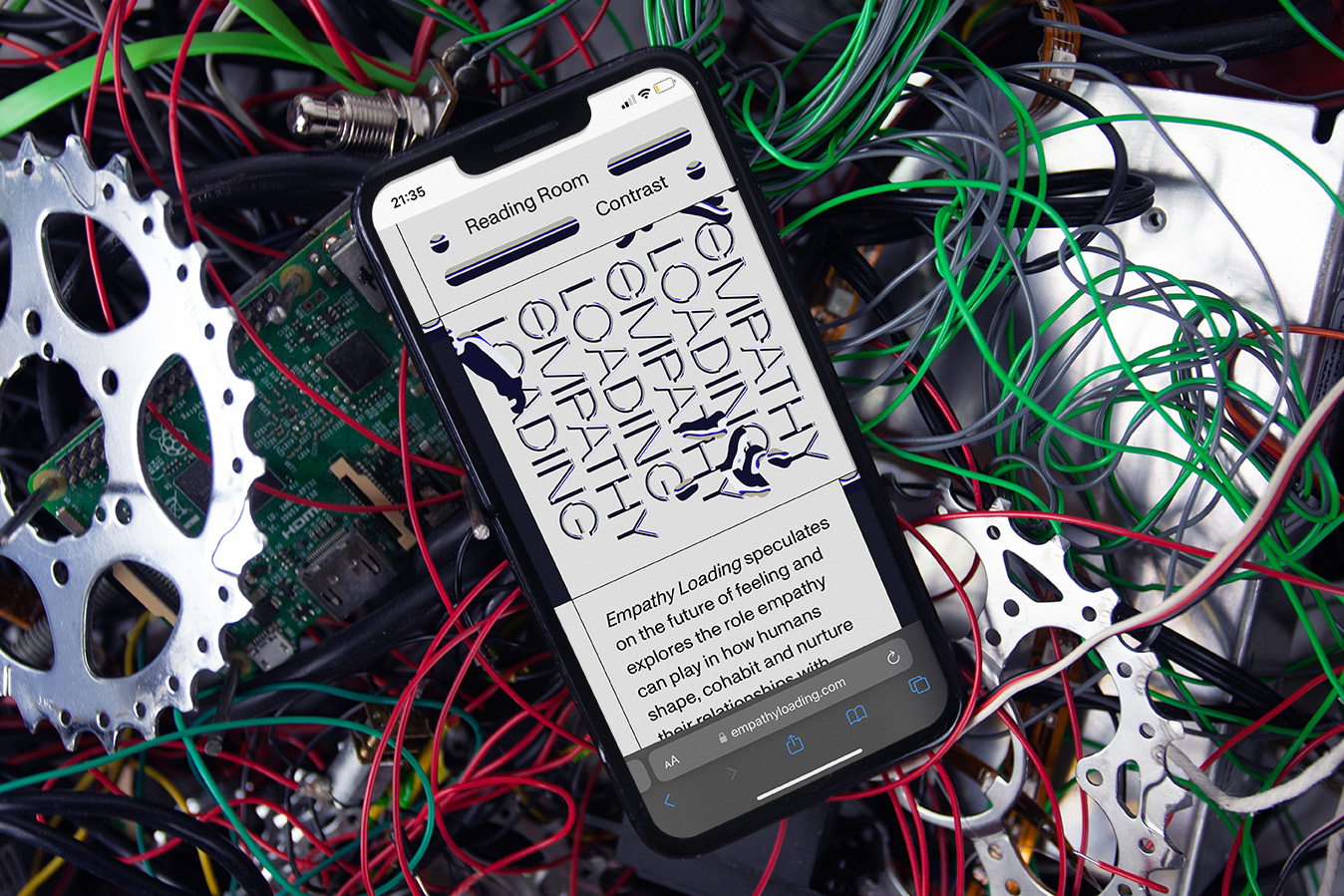 alt: A mobile phone sitting on top of a pile of electroics and wires, displayed on the phone is the Empathy Loading moblie site home page.