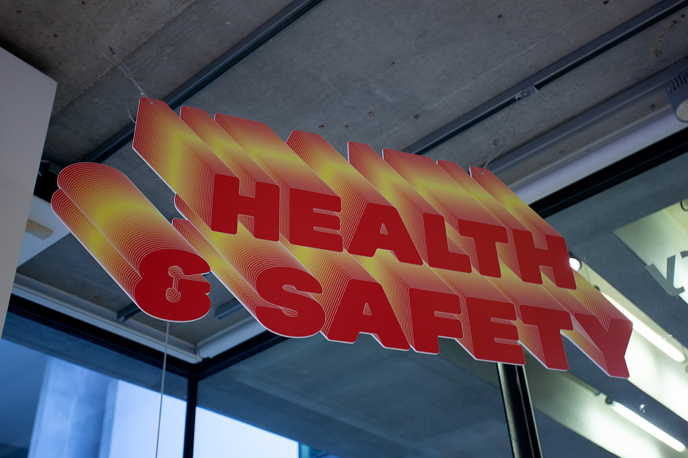 a red and yellow sign reading Health and Safety with a stretched 3D effect, inspired by word art, hanging in the Lethaby Gallery