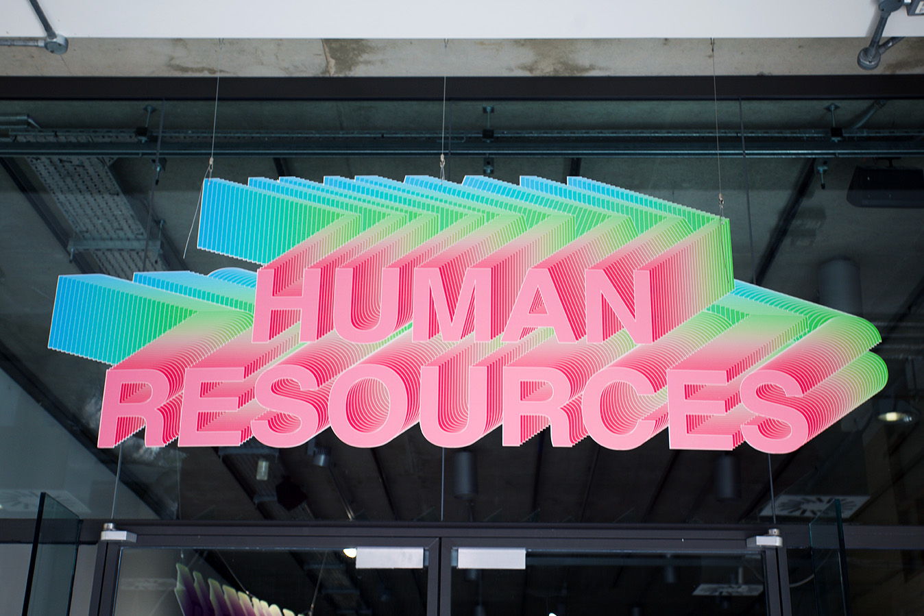 alt: A large sign hanging from a ceiling, the sign, made in response to the provocation of the project, uses clip art styling and layering of the Human Resources title