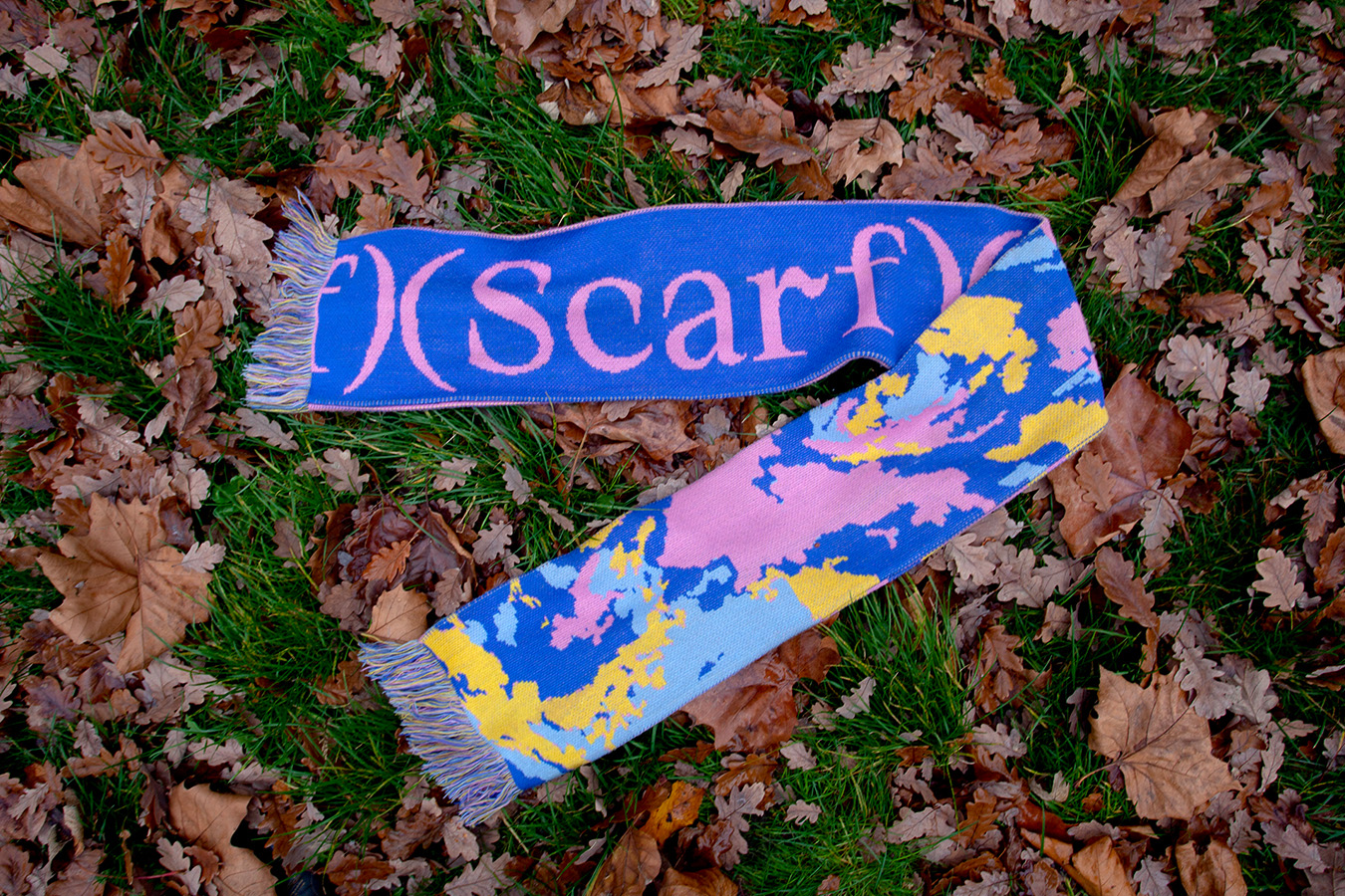 A second image of the scarf, laying on the floor surrounded by scattered leaves
