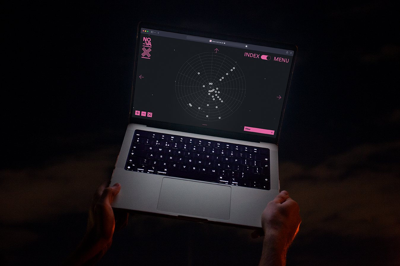 alt: Two hands holding up a laptop in front of the night sky, displayed on the laptop is the Nova X website homepage.