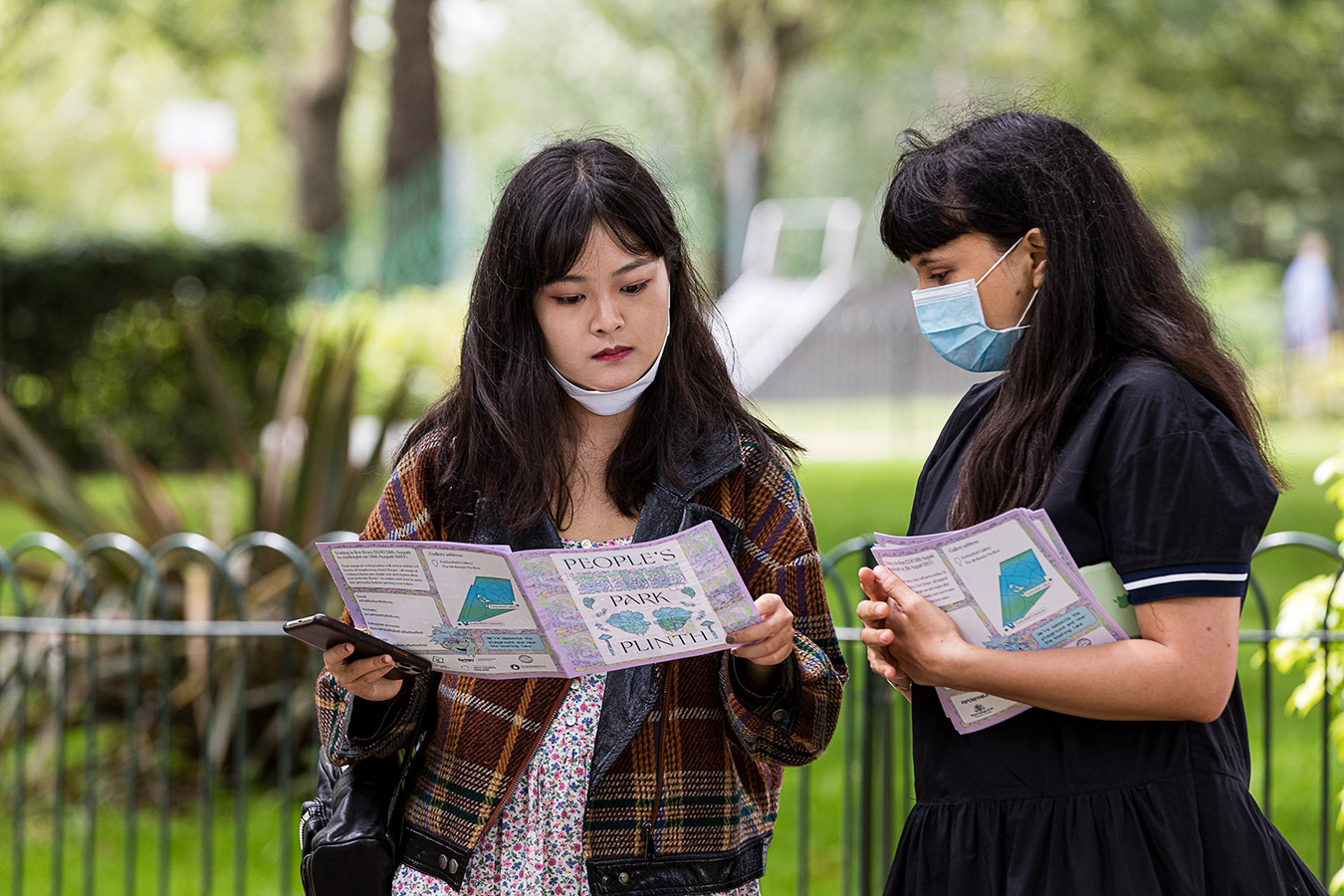 two girls reading the People's Park Plinth booklet in the park
