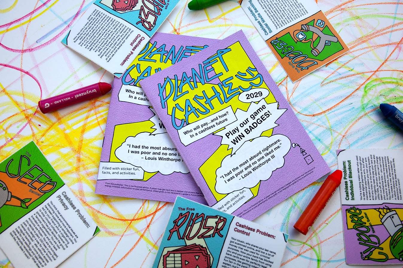 alt: Planet Cashless booklets are laying on a table which has been drawn all over by children, around the booklets crayons and stickers can be seen