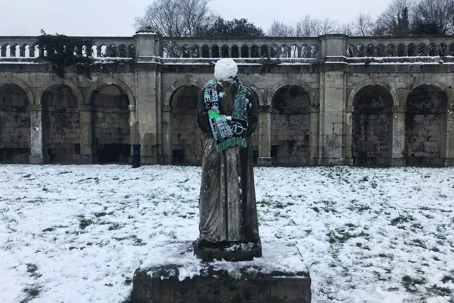 A playful image of the scarf wrapped around a statue on a cold winters day surrounded by snow