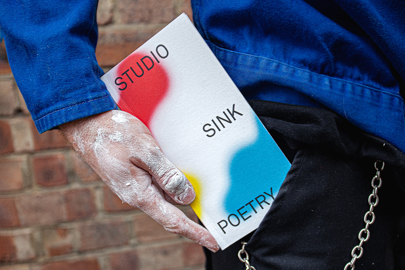 alt: Man holding a book entitled Studio Sink Poetry. The cover has design using red, blue and yellow spray paint