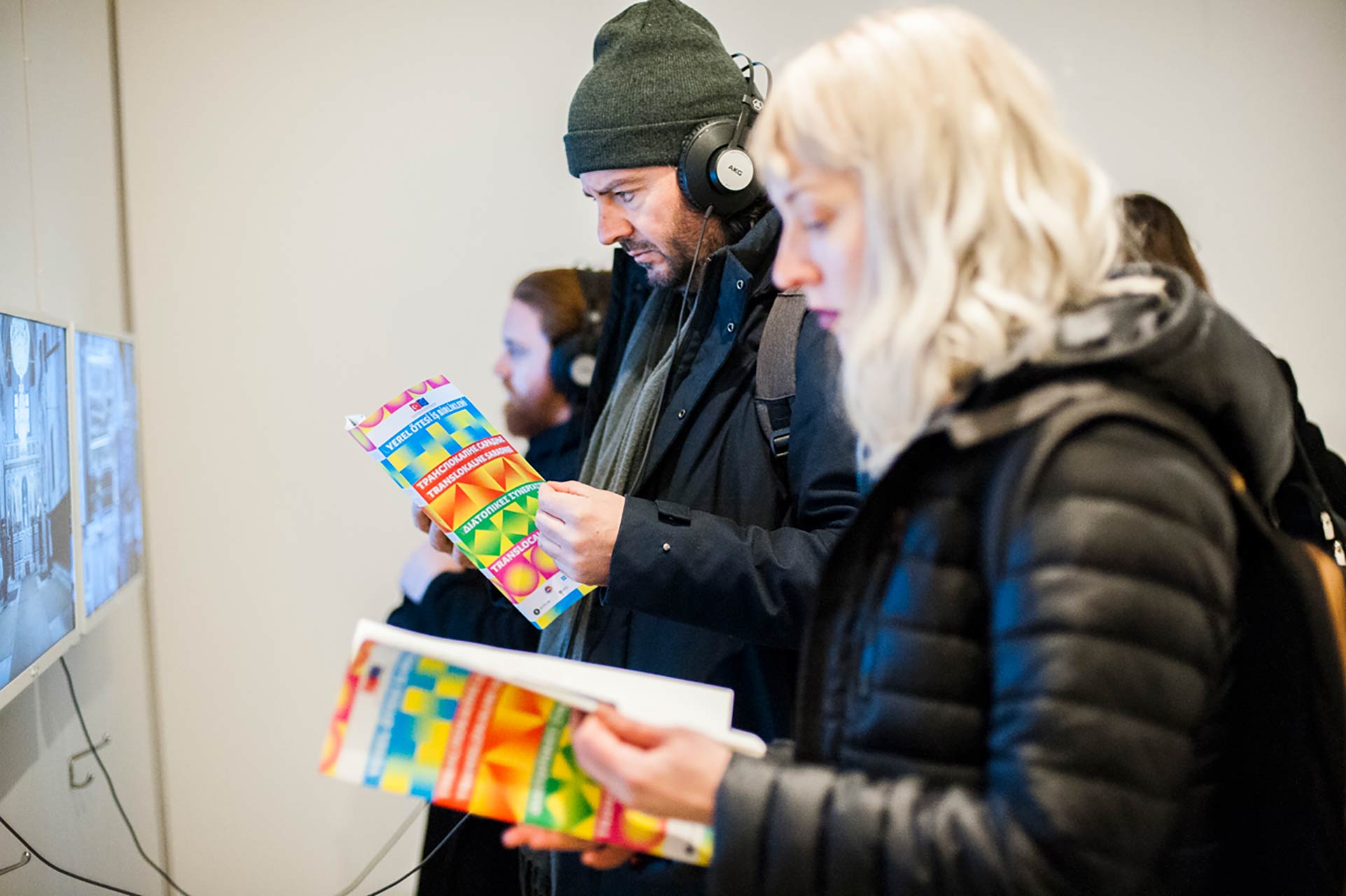 Members of the public are seen watching video artworks, while reading and holding copies of the Trans Local booklet